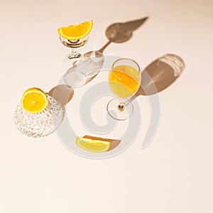 Summer concept made of champagne glasses and a glass jar with lemon and orange slices. Pastel beige background.