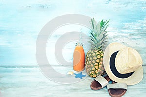 Summer concept stillife - ripe pineapple, straw hat, flip-flops and a bottle of multivitamin juice in front of a blue rustic