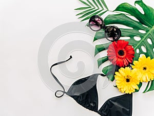 Summer concept. Sunglasses and bikini over tropical leaf monstera with flowers