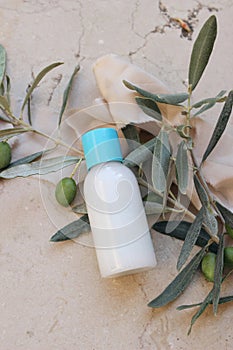 Summer cosmetic still life scene. Oil, shampoo or cream bottle mockup with blue cap. Olive tree branches, fruit on beige
