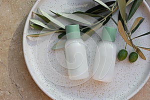 Summer cosmetic still life. White oil, shampoo or cream bottles with green cap. Olive tree branch, fruit and silk ribbon