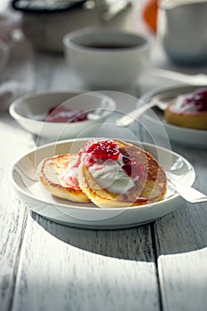 Summer cottage cheese pancakes on white plates on a wooden table with coffee, milk, sour cream and jam, closeup
