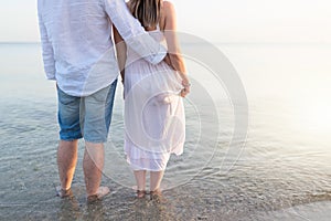 Summer couple embracing at sunset on beach. Romantic young couple enjoying sun, sunshine, romance and love by the sea