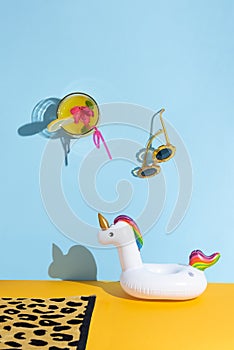 Summer creative concept with a glass of juice, sunglasses, a beach towel and an inflatable reel on a blue and orange