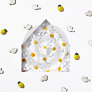 Summer creative minimal still life. White daisy, bird toy and ladybug with house silhouette creative composition. White table with