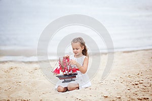 Summer day. Happy childhood carefree game on the open sand. The concept of rest. Girl on the sea with a ship. portrait of the girl