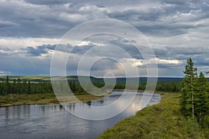 Summer day landscape with river, forest, clouds on the blue sky and sun