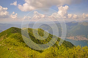 A summer day landscape view of a green valley with a river and green mountains and a blue sky and a small coastal city visible