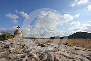 A summer day shot of an old stone cross on the side of a country road with a field with sheep, a hill, a blue sky with white