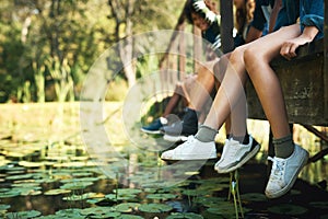 Summer days spent down at the creek. a group of unrecognisable teenagers sitting on a bridge in nature at summer camp.