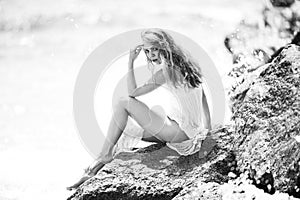 Summer dream. Sexy woman sitting on rocky beach against sea blue waves. Sensual young woman wearing sexy summer dress on