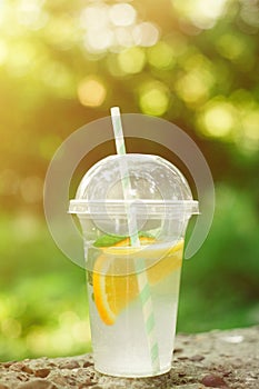 Summer Drink Lemonade with orange and mint in the plastic cup against vivid green background