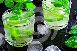 Summer drink Mojito, with lime, mint and ice cubes, on a black background with water drops