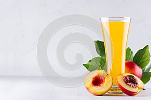 Summer drink - peach juice and red ripe nectarines with leaves and fleshy slice on soft light white wood background.