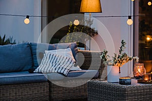 Evening on the terrace of beautiful suburban house with patio with wicker furniture and lights