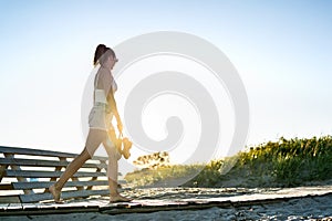 Summer evening walk on the beach boardwalk at dawn. Lonely sad young woman in melancholy or solitude at sunset. Almost silhouette.