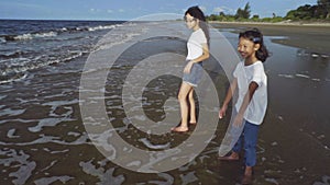 Summer family holidays, vacation concept-two asian teenager sisters standing barefoot in water on beach