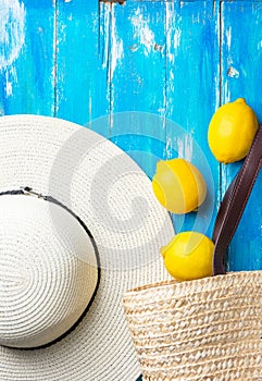 Summer fashion background. Straw hat wicker handwoven beach bag fresh lemons on blue wood. Travel vacation concept. Provence style