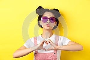 Summer and fashion concept. Cute glam girl with sunglasses and hairbuns, showing heart sign and pucker lips for kiss, I