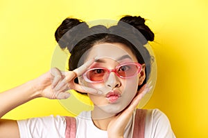 Summer fashion concept. Cute and glamour asian girl in sunglasses, showing v-sign kawaii and looking at camera, standing