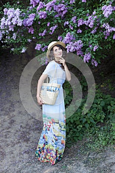 Summer fashion portrait of stunning woman walking in the blooming lilac garden. Wearing long vintage dress. Romantic mood. Secret