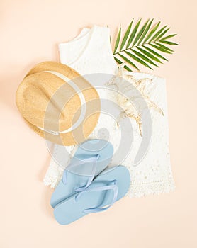 Summer fashion, summer outfit on cream background. White lace dress, blue flip flops, seashell and straw hat. Flat lay