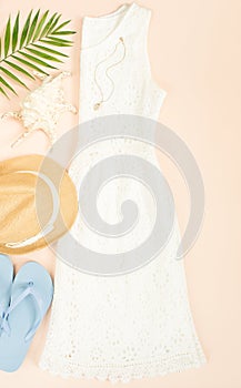 Summer fashion, summer outfit on cream background. White lace dress, blue flip flops and straw hat. Flat lay, top view