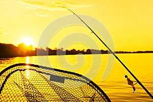 Summer fishing on a freshwater river. Fishing tackle on an orange sunset background