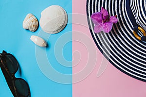 Summer flat lay: orchid flower, sunglasses, shells and a sun hat on a pink-green background.