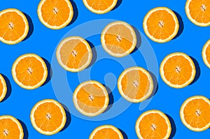Summer flat lay pattern made with fresh orange fruit slices on vibrant blue background. Minimal sunlight concept with sharp