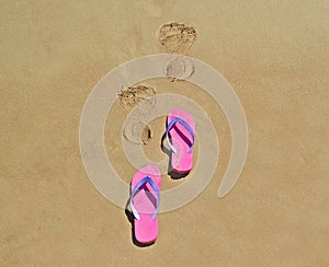 Summer flip flops on the beach with footsteps on sand