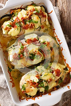 Summer food baked chicken fillet with zucchini, bacon and cheese close-up in a baking dish. vertical top view