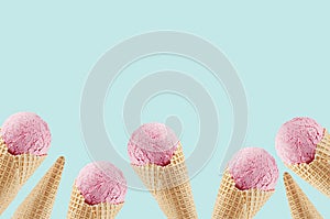 Summer food decorative border of delicious pink ice cream in crisp waffle cones on green background.