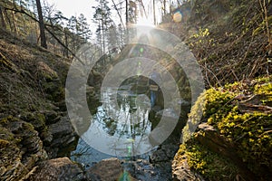 A summer forest. A man going straight in the forest avoiding the river stepping on the rocks