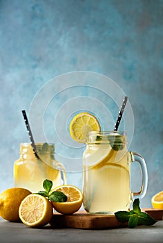 Summer fresh drink with lemons and mint leaves on blue background. Lemonade in jar with straw