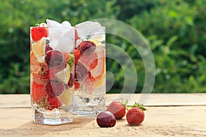 Summer fresh drink with mineral water with ice, berries and fruits strawberry, cherry, lemon, grapefruit on a natural green