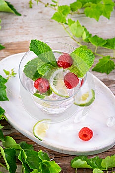 Summer fresh drink. Raspberry mint alcohol cocktail, slice of lime, ice cubes and raspberry on a natural wooden surface, Outdoor.