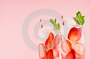 Summer fresh drinks with strawberry, ice cubes, green mint and striped straw on pink wall, closeup, top section, edge.