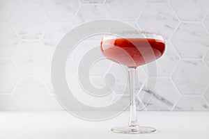 Summer fresh fruit strawberry cocktail of grinded red berry with sugar rim in glass goblen on white wood table with marble tile.