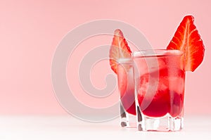 Summer fresh red cocktails in shot glasses with ice cubes, strawberry slice on white wood table and pastel pink wall, copy space.