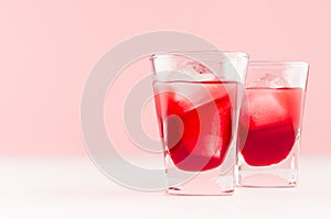 Summer fresh red strawberry drinks with ice cubes in two shot glasses on fashion pastel pink color background and white wood table
