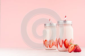 Summer fresh strawberry milkshake in jars with bright fruits, silver caps, red striped straws on elegance pink background.