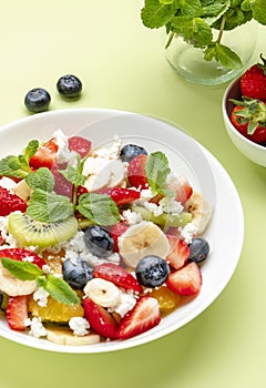 Summer fruit and berry salad with feta cheese, fresh strawberries, blueberries, banana, kiwi, orange and mint, green background,