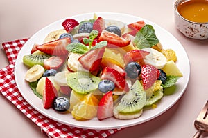 Summer fruit and berry salad with fresh strawberries, blueberries, banana, kiwi, orange and mint, pink background, top view