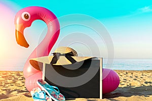 Summer fun beach. Funny pink toy flamingo with blackboard, slippers and hat for text on summer ocean nature beach background in