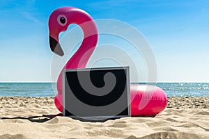 Summer fun beach. Funny pink toy flamingo with blackboard for text on summer ocean nature beach background in sunny