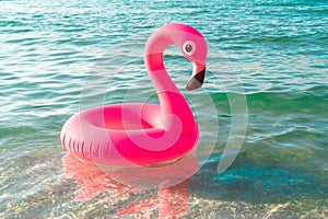 Summer fun beach. Pink inflatable flamingo in blue sea water on summer ocean beach background. Funny bird toy for kids