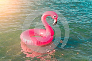 Summer fun beach. Pink inflatable flamingo in blue sea water on summer ocean beach background. Funny bird toy for kids