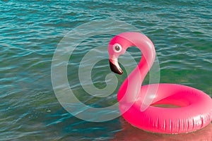 Summer fun beach. Pink inflatable flamingo in blue sea water on summer ocean beach background. Funny bird toy for kids