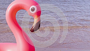 Summer fun beach. Pink inflatable flamingo in blue sea water on summer ocean beach background. Funny bird toy for kids